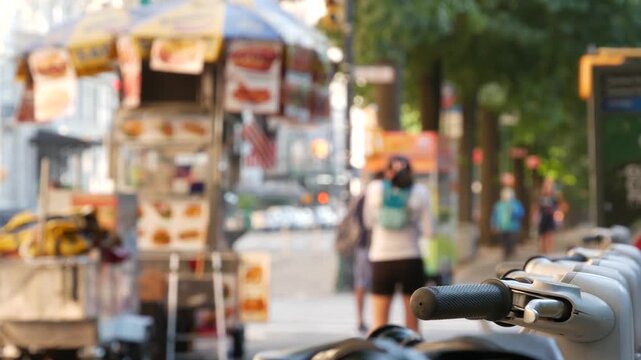 Manhattan Midtown street New York City, United States. Rental bicycle parking, Central Park West summer trees greenery. Bike for rent in row. People pedestrian on sidewalk pavement. Hot dog fast food.