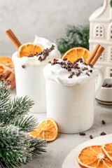 Hot chocolate drink with whipped cream, dried orange and spices in mug on white festive christmas table background