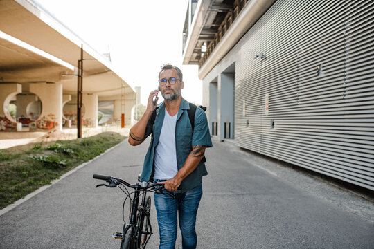 Male cyclist making phone call, standing by his bike.