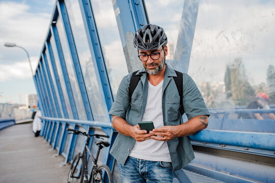 Bearded cyclist using phone while waiting for bus.
