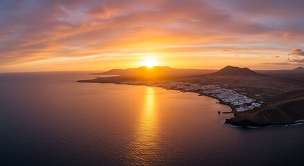 Aerial view of a coastline with a village, ocean, and mountains during a vibrant sunset