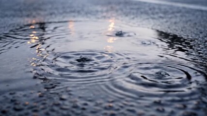 Close-up shot capturing the mesmerizing ripples on a water puddle created by falling raindrops, showcasing the natural beauty of the rain
