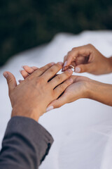 A close-up of two hands during a tender moment, where one person is placing a gold wedding ring on...
