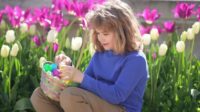 Easter child in blossom spring park. Kid hunting Easter eggs near tulips. Kid play wit Ester eggs outdoor. Kids portrait in garden. Dreamy and surprised child look. Kid play with Easter eggs.