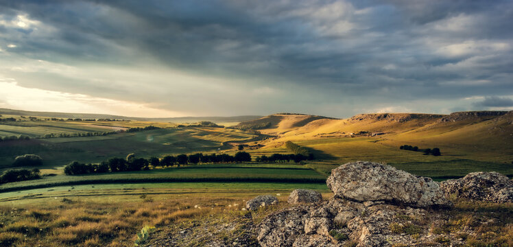Beautiful rural landscape with rolling hills, lush green fields, and dramatic cloudy sky at sunset