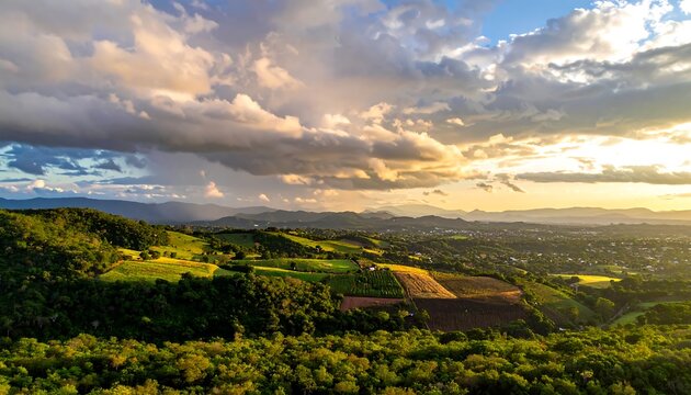 Aerial view of rolling hills with cultivated fields under a dramatic, sunlit, cloudy sky