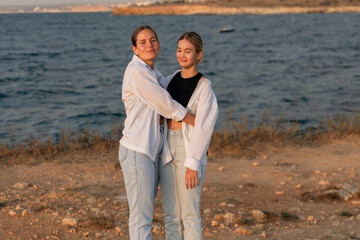 Couple Beach Hug Sunset - A young couple embraces on a beach at sunset, looking out at the sea.