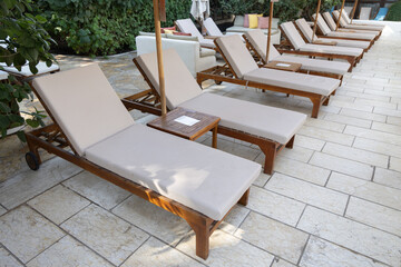A row of comfortable sunbeds lined up by the pool, perfect for lounging and relaxing. The wooden frames and neutral cushions create a stylish and serene outdoor space for leisure