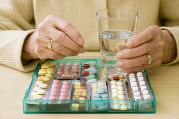 Medication management system for elderly, hands holding water glass near organized pillbox with assorted tablets emphasizing health monitoring and proper dosage