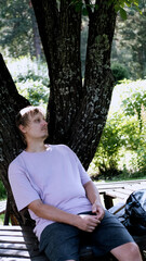 Relaxing man in a park on a bench in summer, enjoying the fresh air, vacation, or relaxing alone in...