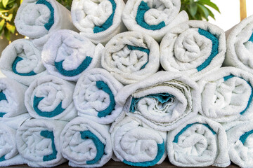 Close-up of neatly rolled white towels with turquoise edges, stacked in pyramid shape. Perfect for...
