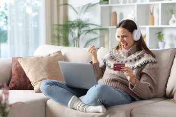 Excited woman in winter buying online media using card at home