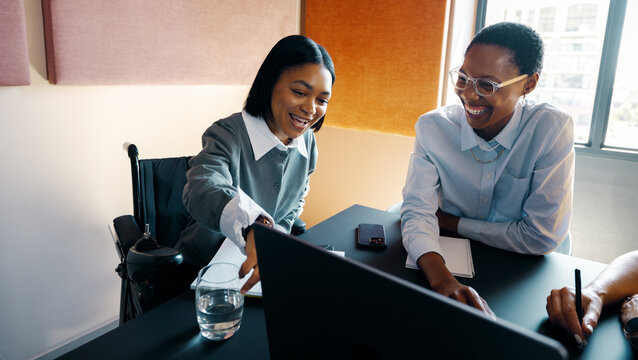 Two young women joyfully working together at an office table