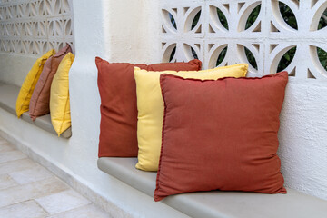 Close-up of vibrant cushions in yellow and orange placed on a stone bench in an outdoor space. The...