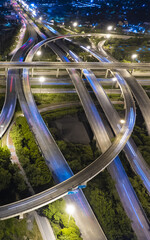 Aerial view of city highway interchange at night with light trails from moving cars, showing modern urban infrastructure and transportation network.
