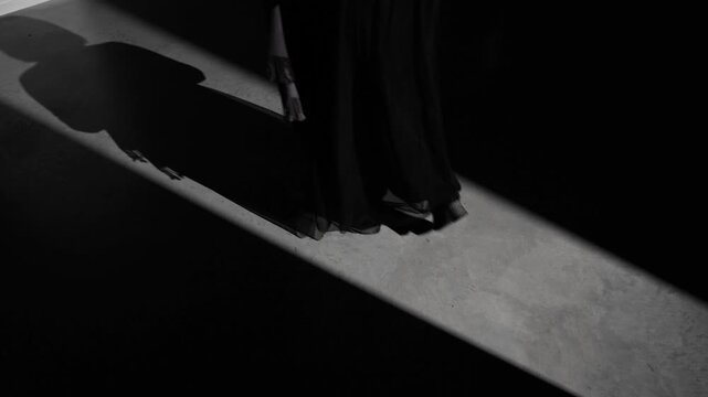 A woman's shadow, partially obscured by flowing sheer fabric, appears on the floor under a beam of light in a dark space. Strong mood and copy space
