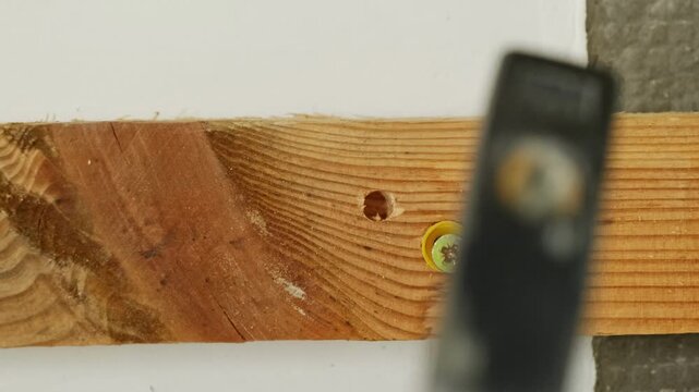 Worker taps with hammer installing nail into wall anchor in wooden plank closeup. Handyman carefully fastens bar crafting plasterboard wall