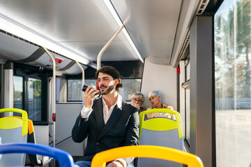 Young man holding and speaking into his smartphone on a public city bus, using a voice assistant while commuting