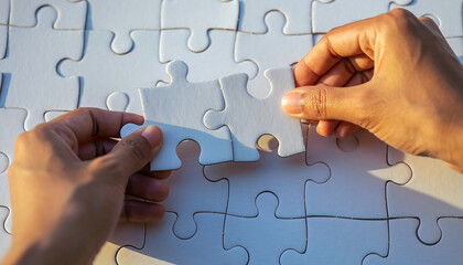 Realistic close-up of two hands joining white puzzle pieces, representing teamwork, unity, and collaboration in a clean minimal background.