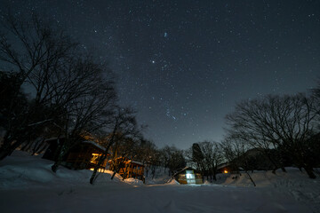 Fototapeta premium 冬の夜、雪原に輝く星と温かい光のキャビン