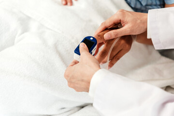 A healthcare professional clips a fingertip pulse oximeter onto a patient's finger, monitoring oxygen saturation and vitals at the bedside.