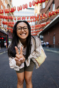 Smiling woman making peace sign in Chinatown street with lanterns
