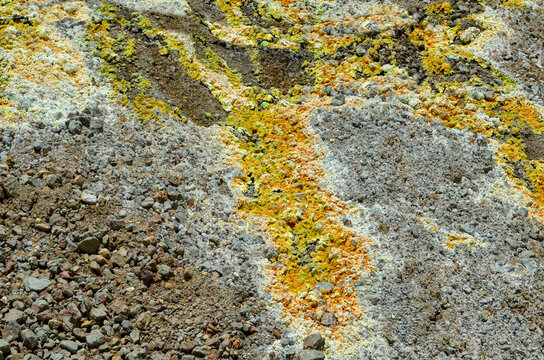 Close-up, abstract detail of rough ground and rubble at mine site, featuring vibrant yellow sulphur and white mineral deposits contrasting with the grey and brown rocks. Geological texture background. - Powered by Adobe