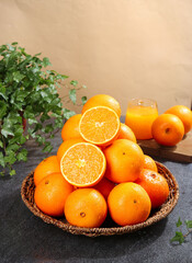 Sweet Navel Oranges in Wicker Basket with Fresh Orange Juice and Green Plant on Dark Slate Surface