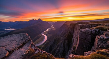 A breathtaking view of a mountain range with a river flowing through it, under a vibrant sunset sky with a mix of warm and cool colors.