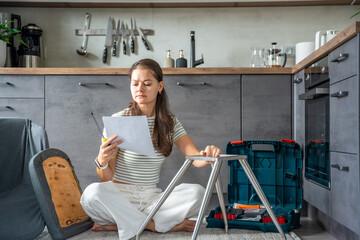 Frustrated young woman sitting on the floor reading instructions while assembling a chair. Concept...