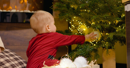 A young mother guides her child as they arrange colorful Christmas balls on a beautifully decorated tree, creating a joyful holiday atmosphere at home.