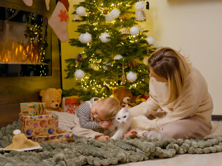 A little boy and his mother share a cozy moment on a blanket by the Christmas tree, engaging with...