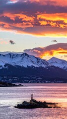 Island lighthouse w/ snow-capped mountains, sunset sky