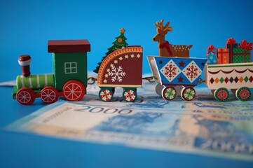 A toy Christmas train and paper bills on a blue background.