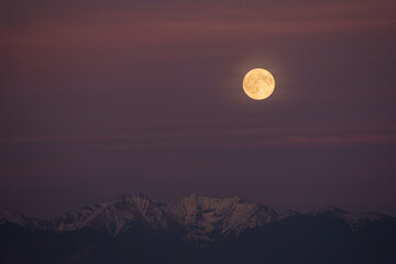Yellow supermoon above snowy Western Tatras during blue hour with a purple-pink evening sky