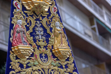 Ornate velvet banner with gold embroidery and religious sculptures during the Virgen del Rosario procession in Granada. Craftsmanship, devotion.