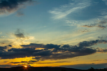 Obraz premium Beautiful sunset with vibrant sky and clouds over rolling hills during golden hour in the countryside
