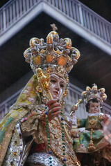 Statue of the crowned Virgin Mary holding the Christ Child during a night procession, richly adorned in embroidered garments and jewelry. Granada, devotion