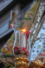 Lit candle in a glass holder with flower petals, captured during a religious procession in Granada, with the Virgin's cloak in the background. faith, ceremony