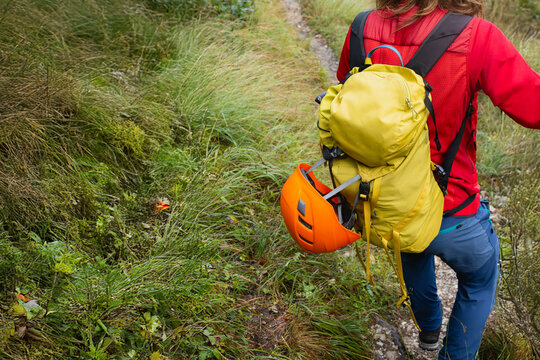 Woman hiker red jacket yellow backpack orange helmet on muddy wet mountain trail. Hiking safety difficult conditions outdoor adventure wild nature