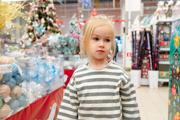 Little child girl shopping in a store with Christmas trees and decorations. Saint Petersburg,...