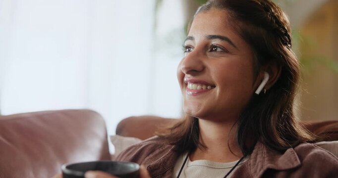 Woman, earphones and thinking in home with coffee drink for streaming podcast for future, planning or idea. Indian person, smile and tea beverage on couch for music subscription, thoughts or relax