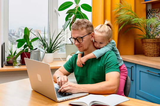 Father works remotely in the kitchen on a laptop, daughter little child distracts attention disturbs parent from work on laptop - Powered by Adobe