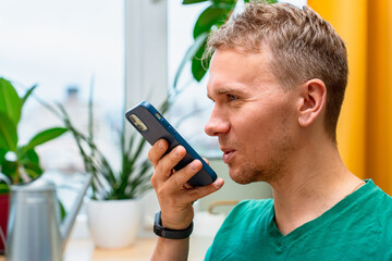 Young man recording voice message with mobile phone or recording note