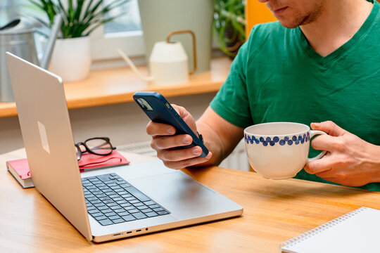 A young man works from home in the kitchen using a laptop. Freelancer working from home