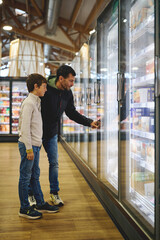Father and son choosing frozen food in supermarket aisle