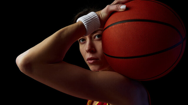Female basketball player posing with ball under dramatic lighting. Concept of power, focus, and intensity for sports campaigns and motivational editorials.