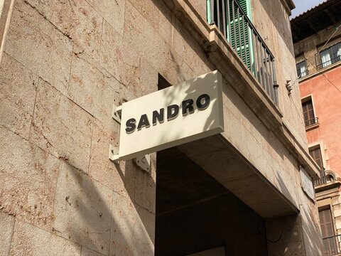 Palma De Mallorca, Spain - October 30, 2025: Sandro brand storefront sign displayed on a textured stone wall in a vibrant urban setting, showcasing modern retail architecture and inviting atmosphere