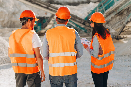 Back view of team of engineers using digital tablet and walking discussing process at mining site