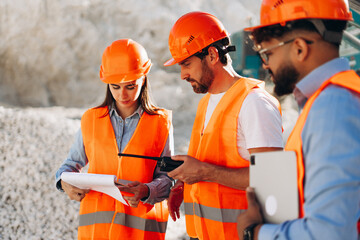 Group of multinational workers wearing orange helmet and vests having discussion at worksite